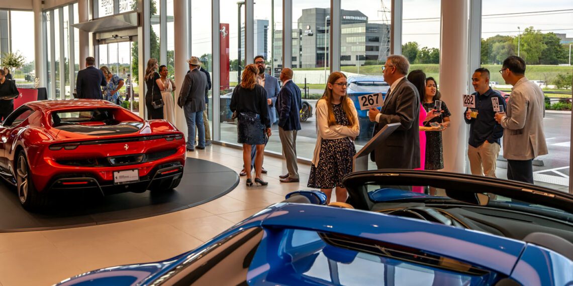 At the Middle Tennessee Gala, people converse at a car dealership event, surrounded by luxury cars. Indoors, natural light from large windows highlights a night where dreams come true.