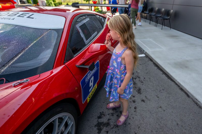 A young girl in a dress eats ice cream while standing next to a parked red sports car with a number 9 decal, capturing the spirit of the Make-A-Wish Gala in Middle Tennessee.