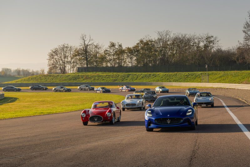 A fleet of sleek sports cars, including a Maserati celebrating its 110 years of Italian luxury, zooms along a racetrack against the backdrop of lush grass and towering trees.