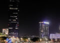 The night view of the cityscape, with tall illuminated buildings reflecting on the water, is enchantingly elegant. A large duck sculpture graces the waterfront, adding a whimsical touch reminiscent of Italian luxury, beautifully highlighting 110 years of artistic inspiration.