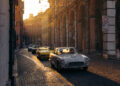 Classic Maserati cars glide over the cobblestone street during sunset, surrounded by historic buildings and arches, embodying 110 years of Italian luxury.