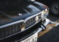 Close-up of a black car's front grille, showcasing the Maserati trident emblem, celebrating 110 years of Italian luxury, with a Japanese license plate partially visible below.