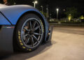 Close-up of a Maserati sports car's front tire with "Pirelli P Zero" branding, parked on a concrete surface at night with streetlights and trees in the background, exuding Italian luxury.