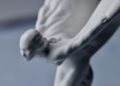 The close-up captures a sleek, abstract, white sculpture resembling a person diving or in motion against a blurred background, reminiscent of the elegance found in bespoke commissions by Rolls-Royce.