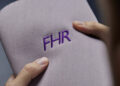 Hands holding a fabric with the letters "FHR" embroidered in purple, reminiscent of the bespoke commissions ethos, akin to the custom elegance one might associate with Rolls-Royce.