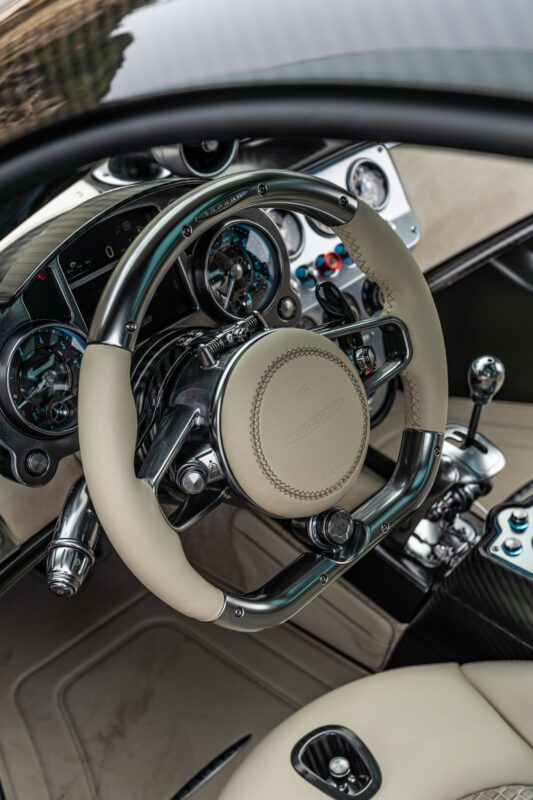 Close-up of a car's interior featuring a luxury steering wheel and dashboard with an analog speedometer and various controls.