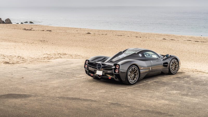 A sleek black sports car parked on a sandy beach with the ocean in the background.