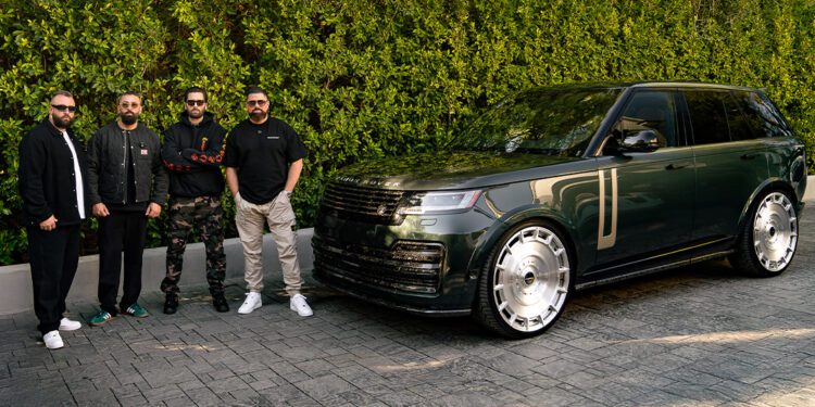 Four people stand next to a sleek black Range Rover L460 on a paved driveway, with lush greenery in the background.