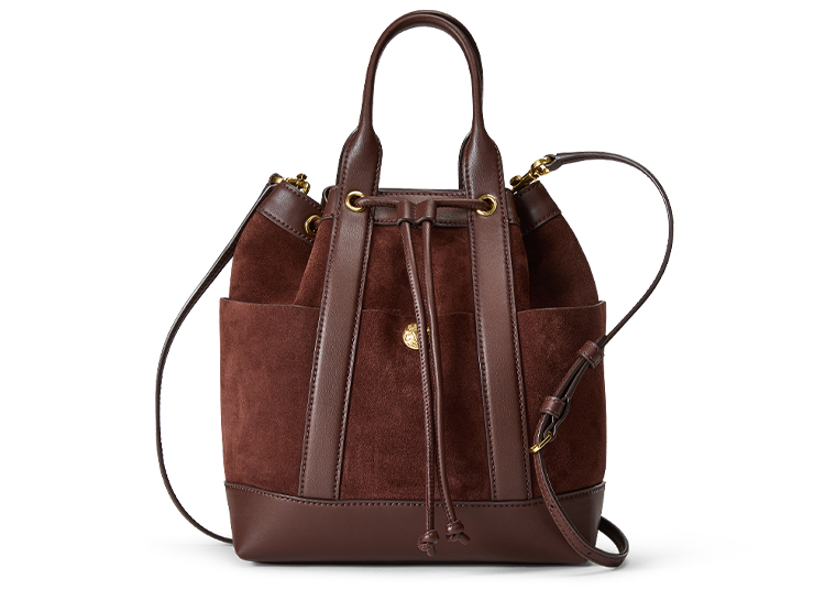 Discover the perfect addition to any 2024 Holiday Gift Guide with this brown suede and leather bucket bag. It features a drawstring closure, top handle, and detachable shoulder strap, making it both stylish and versatile for any occasion.