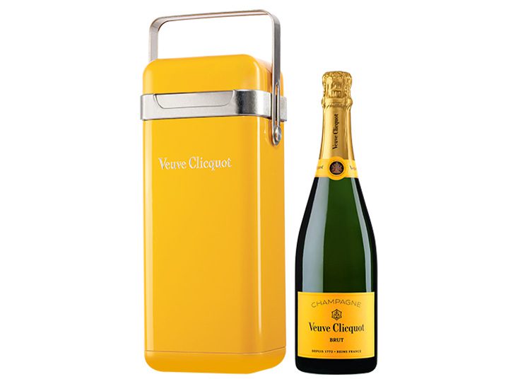 A bottle of Veuve Clicquot champagne stands next to a yellow Veuve Clicquot cooler, perfect for the discerning buyer from the duPont REGISTRY's 2024 Holiday Gift Guide.