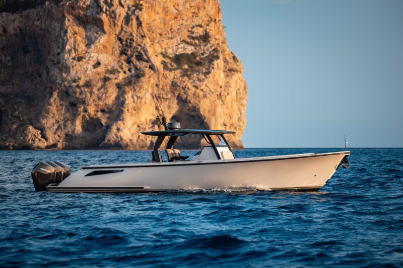 A luxury motorboat from Wajer Yachts cruises on clear blue water near a rocky cliff under a clear sky, showcasing innovation at its finest.