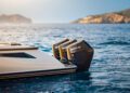 A luxurious Wajer Yacht glides on the water, powered by three innovative Mercury outboard engines, near a rocky coastline beneath a clear sky.