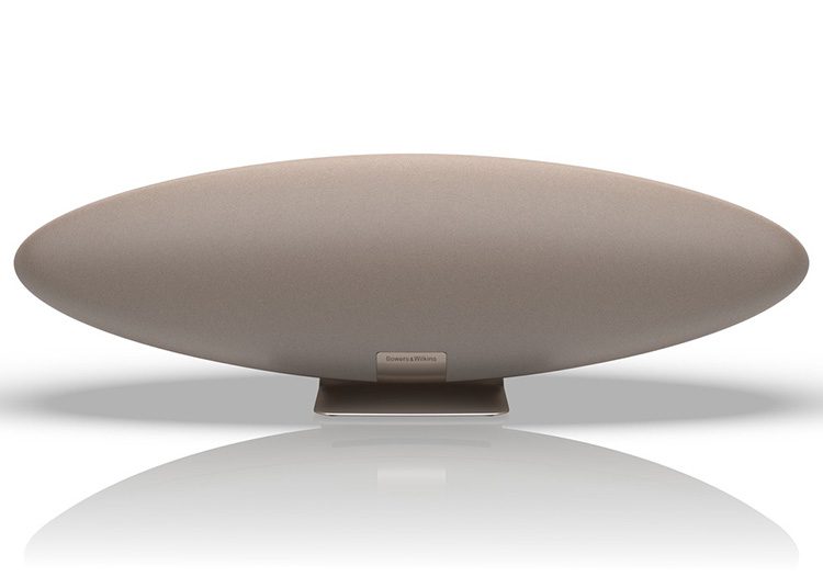 A sleek, oval-shaped wireless speaker in beige, standing on a reflective surface, perfect for this season’s Holiday Gift Guide.