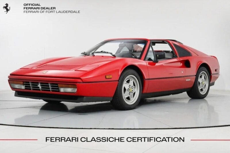 A red Ferrari 328 GTS sports car gleams in the showroom, proudly displaying its Ferrari Classiche Certification at the bottom—a testament to its value as both an automotive masterpiece and a savvy investment.