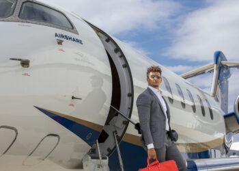 A person in a gray suit, embodying the elegance of an Airshare MVP, carries a red bag as they exit a private jet on a sunny day.