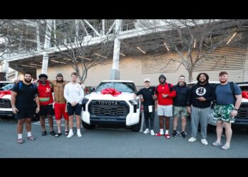 A group of nine people, including NFL QB Brock Purdy, stand proudly in front of a row of white Toyota TRD Pros with red bows on the hoods, posing for a photo outdoors.