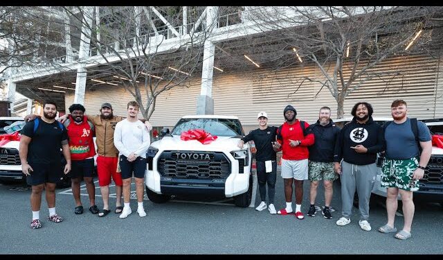 A group of nine people, including NFL QB Brock Purdy, stand proudly in front of a row of white Toyota TRD Pros with red bows on the hoods, posing for a photo outdoors.