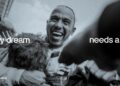 Smiling racer in PETRONAS gear surrounded by team members; text reads "Every dream needs a team." With Lewis Hamilton and the Mercedes crew, it's more than just racing—it's a shared journey.