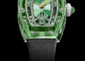 The RM 07-02 from Richard Mille’s Sapphire Collection features a luxury watch with a transparent green case, intricate dial, gold hands, and a black strap against a black background.