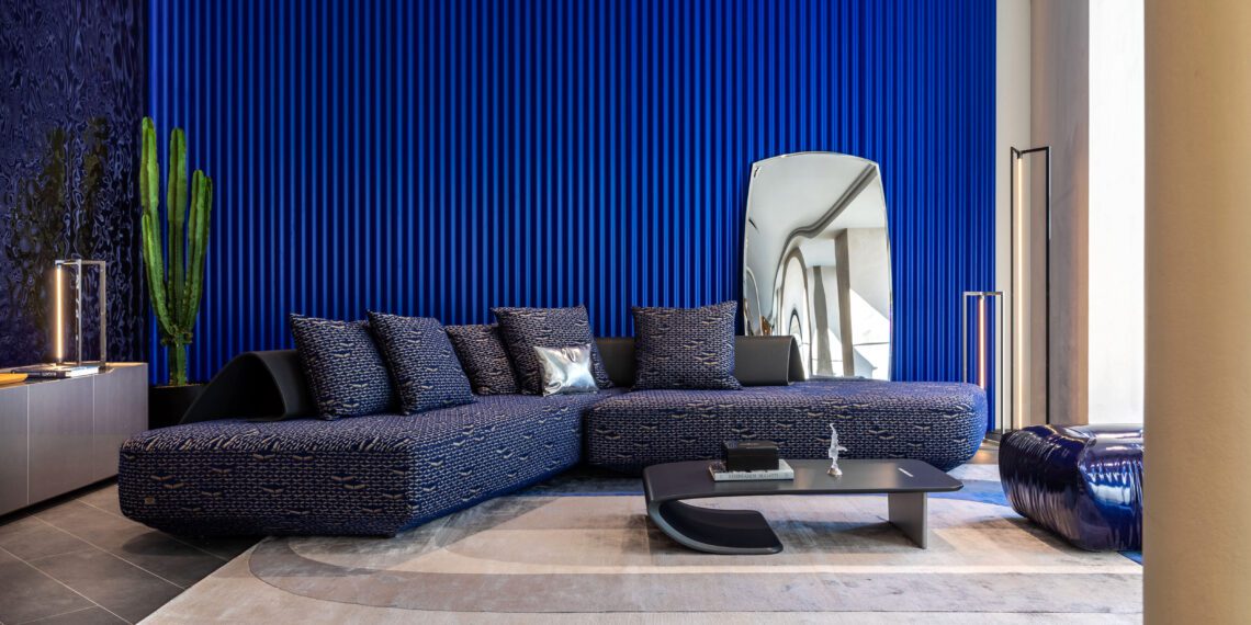 Modern living room with a blue sectional sofa, textured blue wall, cactus plant, abstract mirror, and minimalist decor on a neutral rug from the Paris Home Collection.