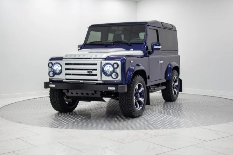 A blue and silver SUV, a unique creation with remarkable off-road capabilities, is parked in a circular white showroom.