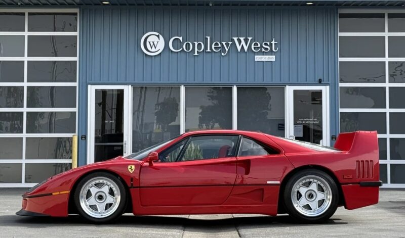 A sleek, exotic red sports car is elegantly parked in front of the CopleyWest dealership, drawing attention to its luxurious design and hinting it's a coveted car for sale.