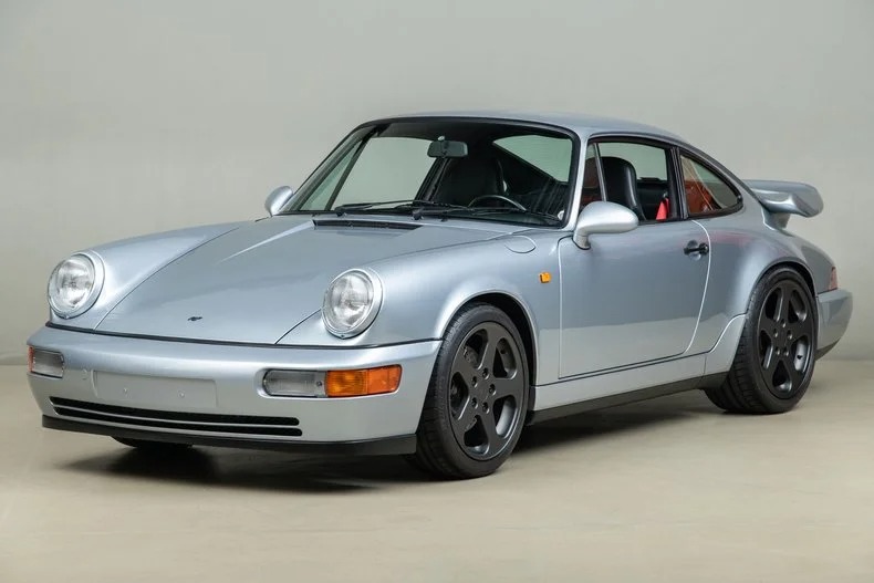 Silver classic Porsche 911 coupe with black wheels and a rear spoiler, viewed from the front left against a plain light background—pure nostalgia for fans of iconic 90s cars for sale.