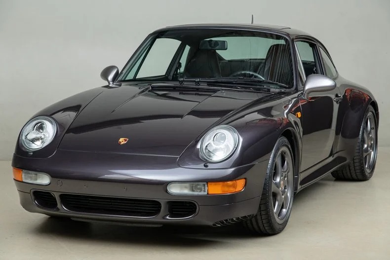 A dark gray Porsche 911 sports car, a classic car evoking nostalgia, is viewed from the front left and parked indoors under soft lighting.