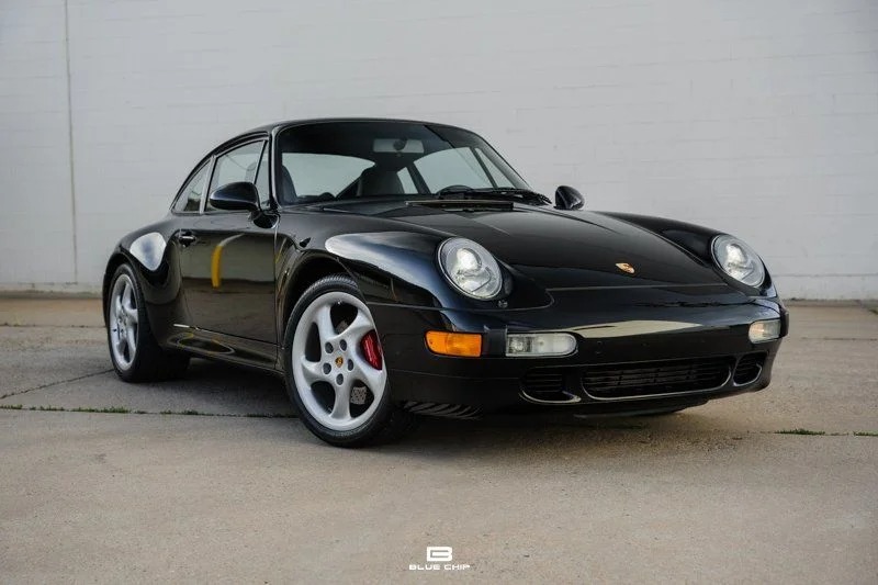 Luxury black sports car parked on a concrete surface with a sleek white wall in the background.