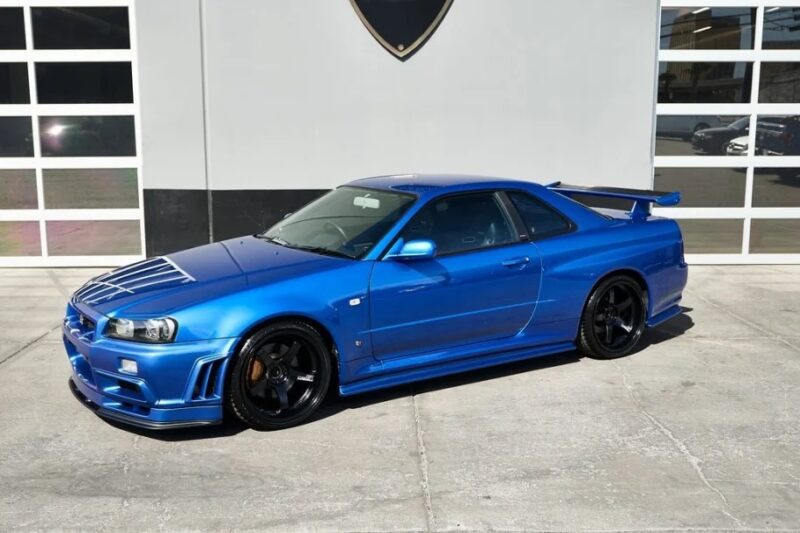 A luxury blue sports car is elegantly parked in front of a building with large windows, showcasing its exotic allure.