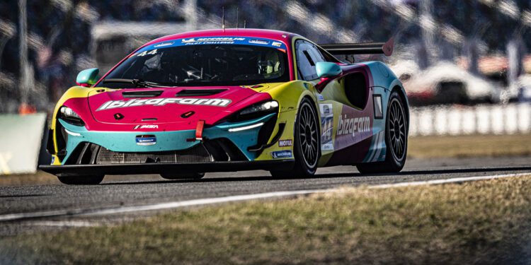 The vibrant McLaren Artura GT4 with "IbizaRam" branding speeds along the track, hinting at its future triumph at the 2025 24 Hours of Daytona. Blurred backgrounds and fencing frame its electrifying presence.