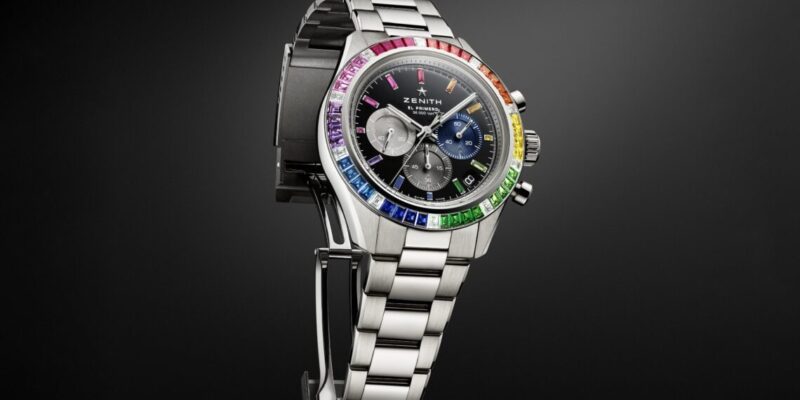 Silver wristwatch with a black face, three subdials, and a rainbow-colored bezel exudes luxury as it's displayed on a stand against a dark background, perfectly capturing the essence of high-end lifestyle products.