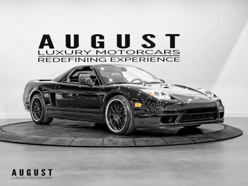 A sleek black luxury car is displayed on a rotating platform in a showroom, with "August Luxury Motorcars: Redefining Experience" written on the wall behind it.