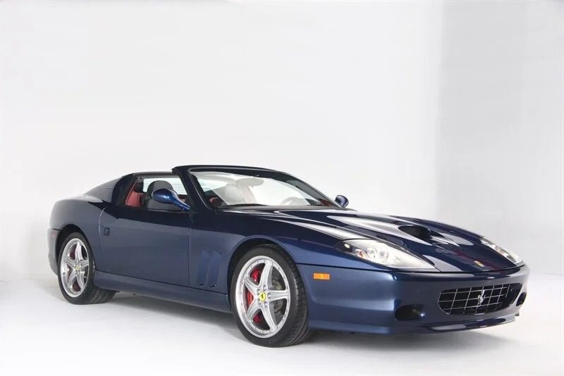 A blue sports car with a convertible top, red interior, and silver alloy wheels sits elegantly in a white studio environment, embodying the allure of exotic cars.