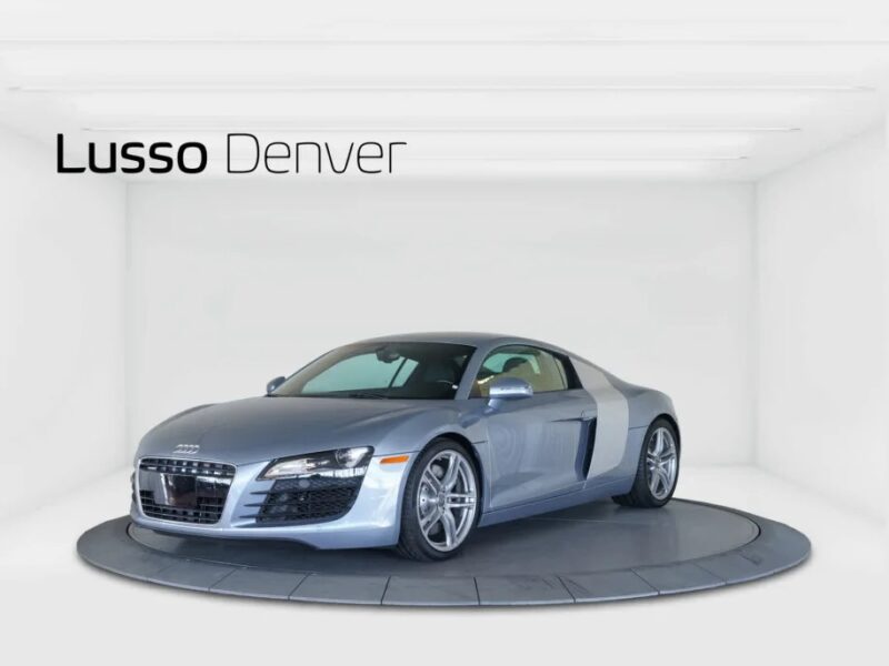 Silver Audi R8 displayed in a bright room with “Lusso Denver” text above, showcasing its allure as a luxury car.