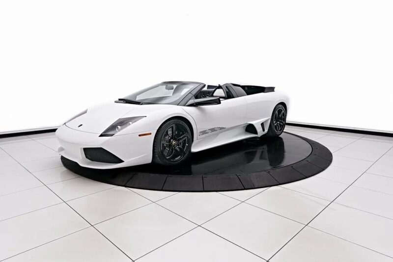 A white convertible sports car, the epitome of an exotic car, is elegantly displayed on a circular platform in a showroom setting.