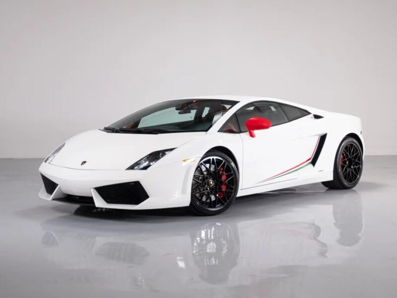 For sale: Stunning white V10 supercar with a red side mirror, black wheels, and elegant green and red detailing. This Lamborghini Gallardo is parked in a well-lit indoor space, ready to impress its next owner.
