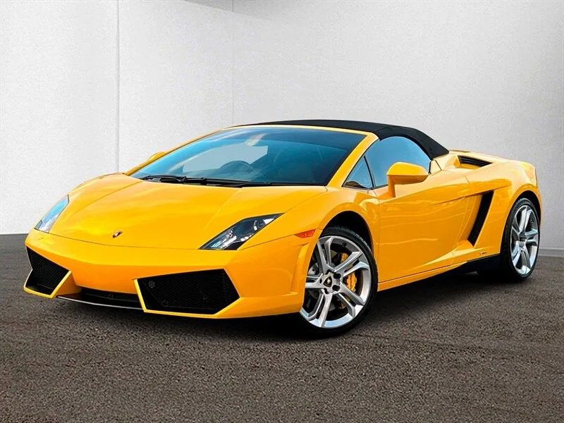 Yellow Lamborghini Gallardos with a convertible top gleam under the sun, parked on textured pavement before a plain white wall. This V10 supercar is now available for sale, offering an exhilarating driving experience wrapped in sleek design.