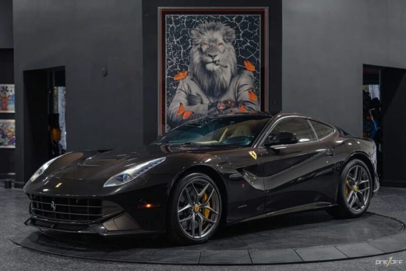 A sleek black sports car with a powerful V12 engine is displayed indoors, complemented by a large framed picture of a lion in the background. This exotic car is an eye-catching masterpiece for sale.