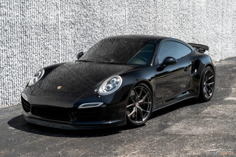 An exotic black sports car is parked in front of a textured wall, exemplifying luxury and style.