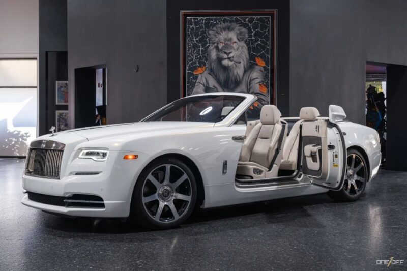 White luxury convertible car with open doors in a showroom, showcasing its beige interior. A large painting of a lion adds to the allure of this exotic car, which boasts the thrill of V12 engines in its powerful heart.