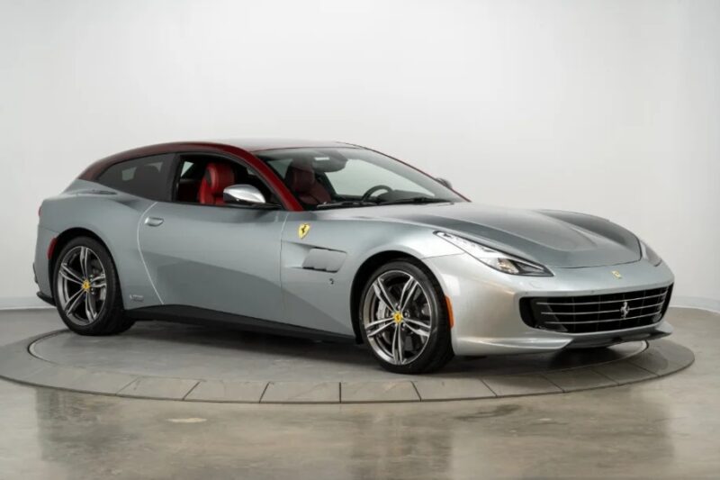 A silver Ferrari GTC4Lusso with a striking red interior graces the showroom, perched on a circular platform. This exotic car, boasting a formidable V12 engine, captures attention and exudes unparalleled luxury and performance.