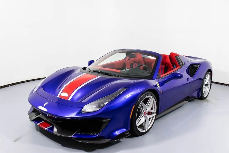 A blue sports car with red and white racing stripes, featuring a convertible top and red interior, is showcased in a plain white room. This exotic car captures attention and is a true gem for enthusiasts seeking luxury cars.