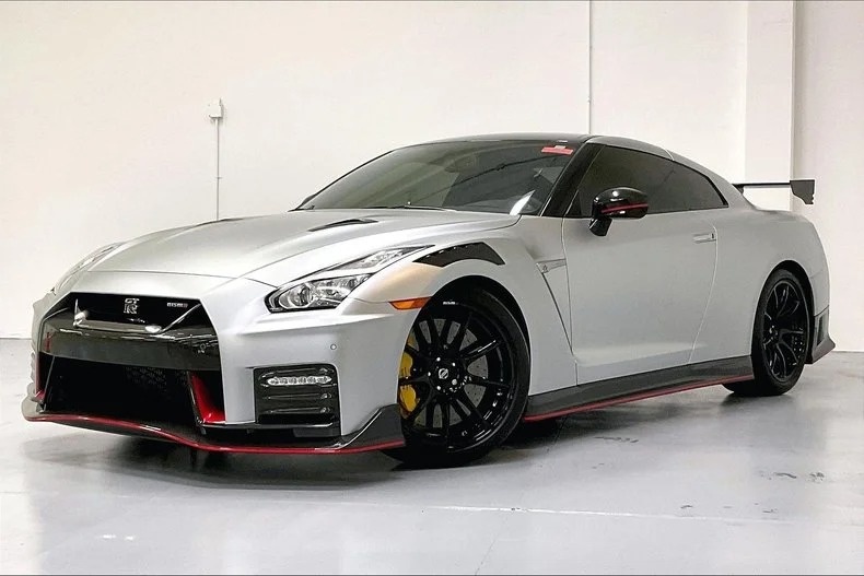 A striking silver sports car with black and red accents, this exotic luxury car boasts a prominent front grille, hood vents, and a rear spoiler. It's showcased in a well-lit indoor space, perfect for discerning enthusiasts browsing exclusive car listings.