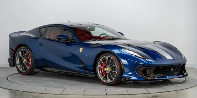 A Blu America Ferrari 812 Competizione with striking red brake calipers is parked indoors on a circular platform against a plain white background, highlighting this stunning sports car now for sale.