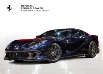 A sleek, dark-colored Ferrari 812 Competizione sports car, possibly in Blu America, is displayed on a reflective surface. The background features the text "Official Ferrari Dealer Ferrari Lake Forest," hinting that this masterpiece might be for sale.