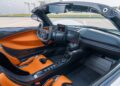 Inside the Hennessey Venom F5, a luxury roadster, you'll find orange and black seats and a sleek dashboard adorned with multiple digital displays. The steering wheel is bejeweled with controls. With its top open, this Heritage Series marvel boasts elegance even while parked outside.