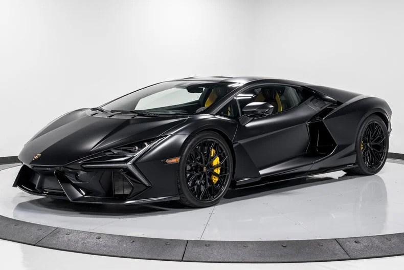 In a well-lit showroom, a sleek, black Lamborghini Revuelto sports car is displayed, flaunting its aerodynamic design and yellow brake calipers. Consider this your moment to buy the 2024 Lamborghini you've always dreamed of.