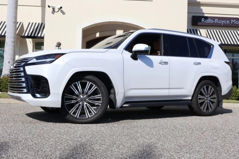 A white luxury SUV, an exotic car that epitomizes sophistication and style, is parked on a street in front of a building.