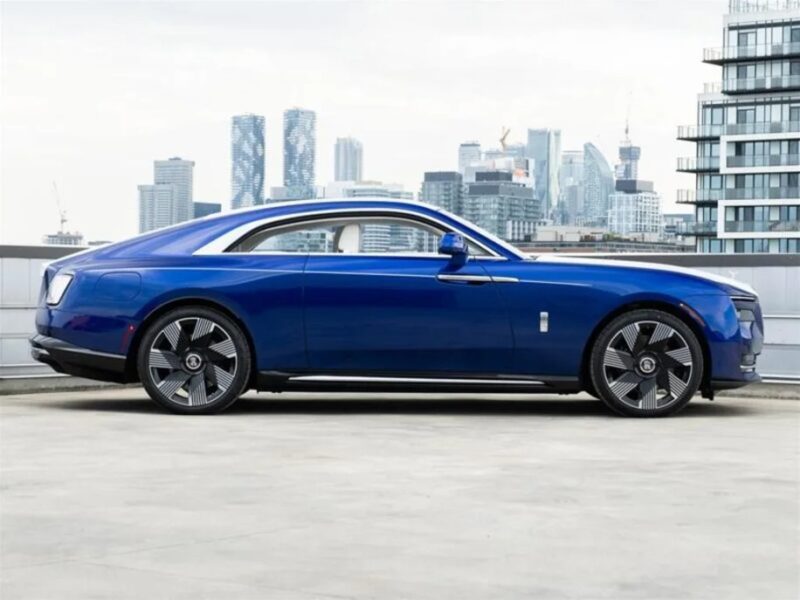 A sleek blue Electric Super Coupe is elegantly parked on a rooftop, with modern city buildings providing a stunning backdrop.